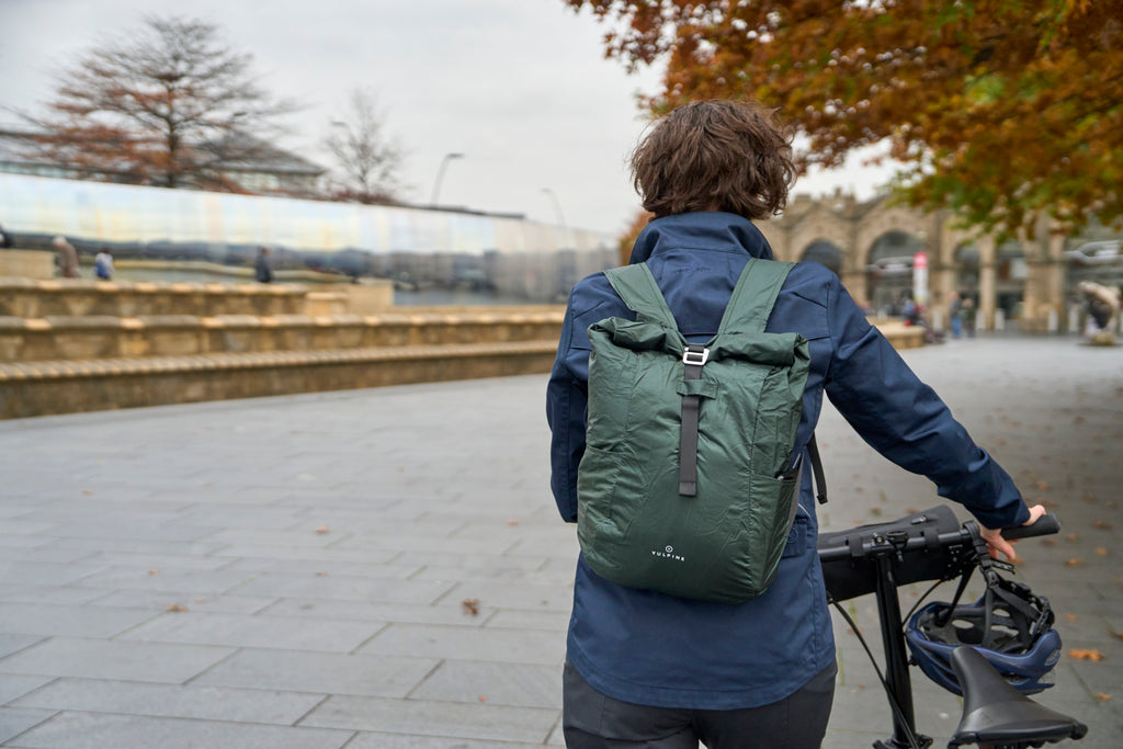 Cyclist wearing a green Finnieston packable backpack while walking with a folding bike