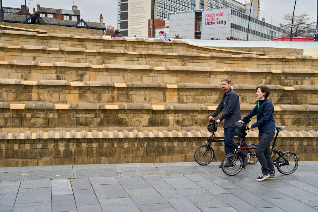 Two cyclists walking their bikes in the city wearing navy Harrington jackets