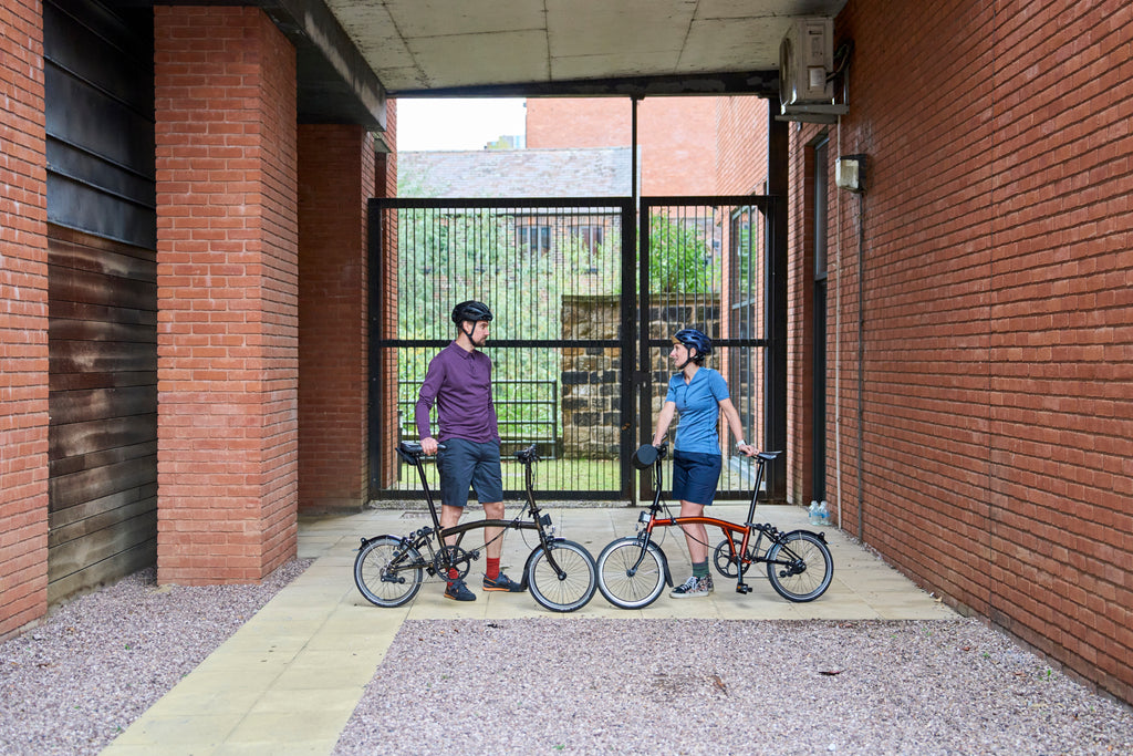 Two cyclists standing with folding bikes, wearing rain shorts