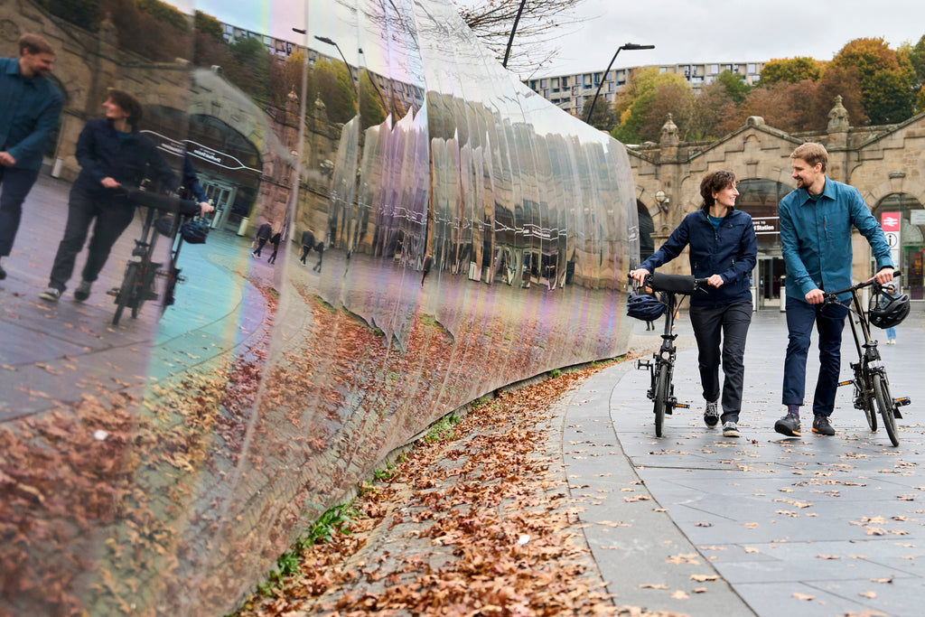 Two people walking bikes beside a reflective wall
