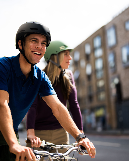 Two people riding bicycles on a street with buildings in the background
